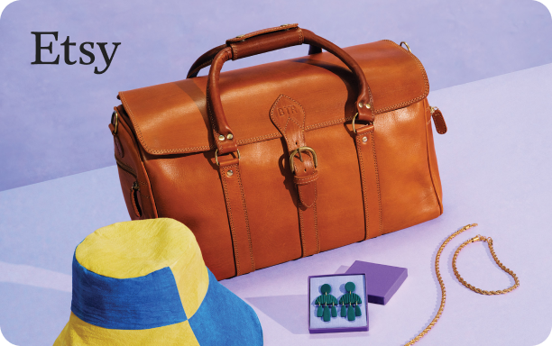 Still life photograph of a brown leather travel bag, yellow and blue panelled bucket hat, a set of dark emerald coloured tiered earrings in a purple jewellery box, and a gold braided necklace and bracelet set on a lavender background with a small Etsy logo in black font in the top left corner